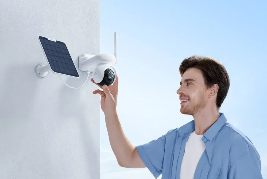 Un homme oriente la tête de la Reolink Altas PT Ultra fixée sur un mur blanc, son panneau solaire posé juste à côté