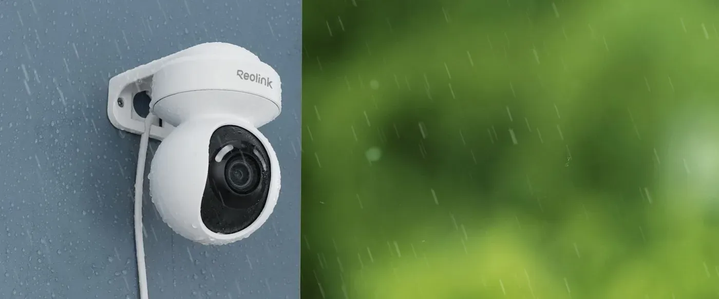 La Reolink E1 Outdoor Pro fixée sur un mur gris, couverte de gouttes pendant une averse